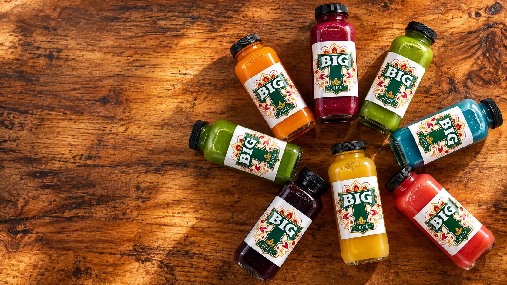 Colorful BIG T Juice bottles arranged on a warm wood table